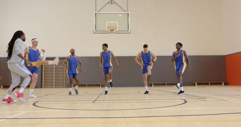 Basketball Team Guided by Coach Warming up in Gym