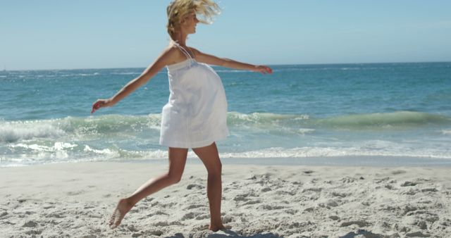 Pregnant woman joyfully dancing and enjoying time on a sandy beach. Ideal for content related to maternity, pregnancy, relaxation, beach activities, summer vacations, and healthy lifestyles.