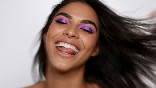Smiling model wearing vibrant purple eyeshadow with flowing dark hair and radiant skin