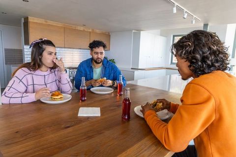 Multicultural friends sharing burgers and sipping red soda at modern kitchen island
