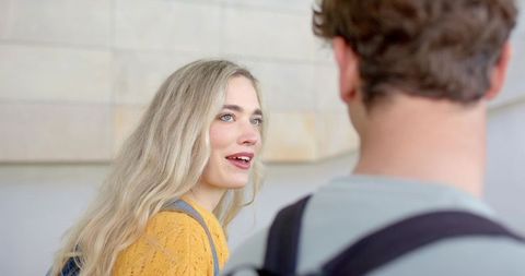 Blonde woman smiling and talking with friend in bright lobby wearing backpack