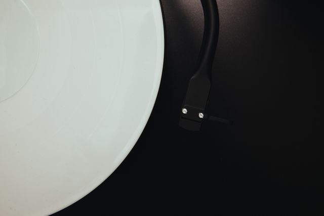This image features a close up of a retro vinyl record player, capturing the spinning record and turntable arm against a dark background. Perfect for use in articles on vintage music technology, retro music collections, or advertisements for audio enthusiast products.