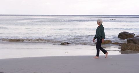 Active Senior Woman Walking On Calm Beach Day Near Ocean