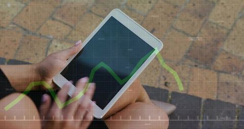 Holding and tapping tablet outdoors showing green financial analytics graph overlay