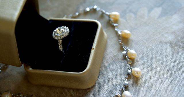 An elegant diamond ring is showcased inside a jewelry box, accompanied by a pearl necklace on a luxurious fabric surface. The image captures the essence of sophisticated jewelry, often associated with special occasions like engagements or anniversaries.