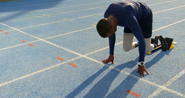 African American man positioned at the starting line on a track field. He's focused on the upcoming sprint, embodying determination and athleticism.