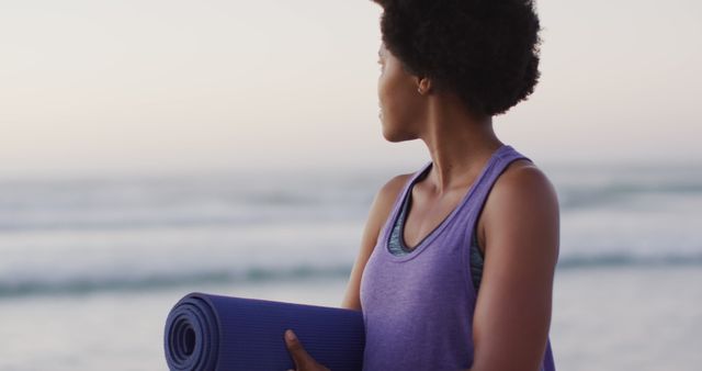Portrait of happy african american woman with yoga mat on sunny beach. healthy and active time beach holiday.