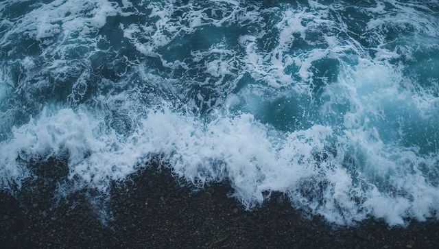 Aerial crashing turquoise waves and foamy surf rolling onto pebble shoreline