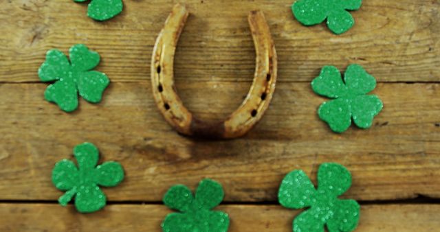 A rusty horseshoe is surrounded by green shamrock decorations on a wooden background, symbolizing luck and the celebration of St. Patrick's Day. The arrangement of shamrocks and the horseshoe creates a festive atmosphere for the Irish holiday.