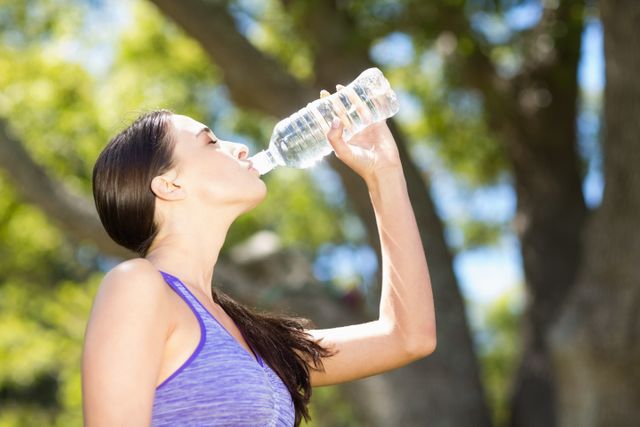Woman staying hydrated while enjoying outdoor activities in a park. Ideal for promoting healthy lifestyle, fitness, and wellness. Suitable for use in advertisements for water bottles, fitness gear, or health-related campaigns.