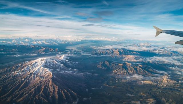 Flying above snow-capped mountain range with winglet over alpine lakes at sunrise
