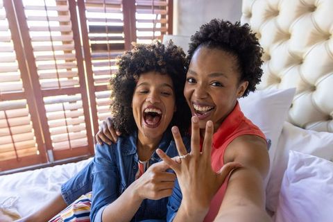 Joyful black female couple celebrating engagement, showing ring in sunlit cozy bedroom
