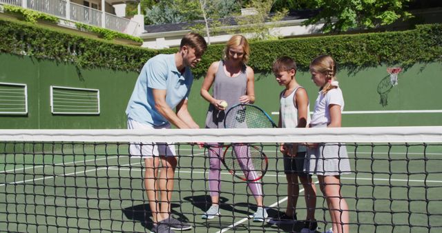 Caucasian father and mother teaching their kids to play tennis at tennis court on a bright sunny day. family, love and sports concept