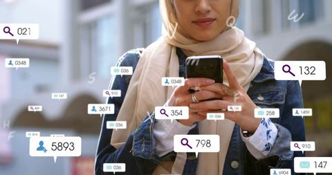Young woman in hijab using smartphone with social media notification overlays in city