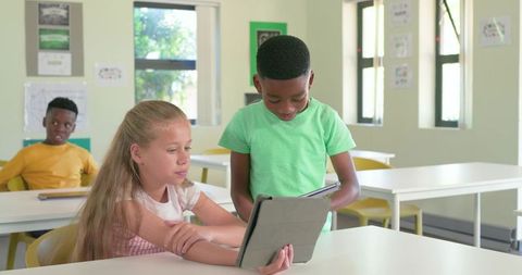 Diverse students collaborating with tablets for digital learning in bright school classroom