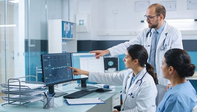 Clinical team reviewing ecg waveforms on dual monitors, collaborating on patient monitoring