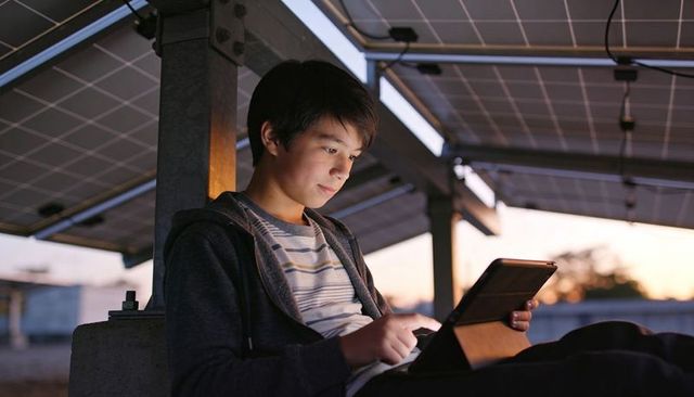 Teen using tablet under rooftop solar panels at dusk showing focused study and tech use
