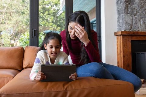 Asian mother and daughter using tablet on leather sofa at home, learning and bonding over educationa