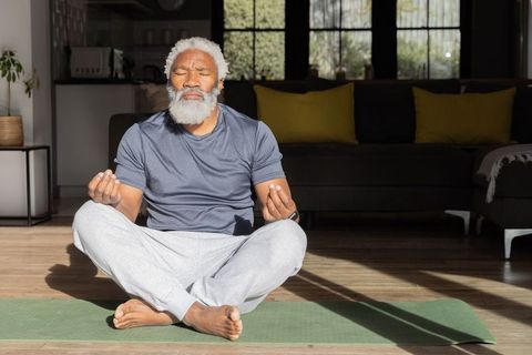Senior african american man meditating on yoga mat in sunlit modern living room
