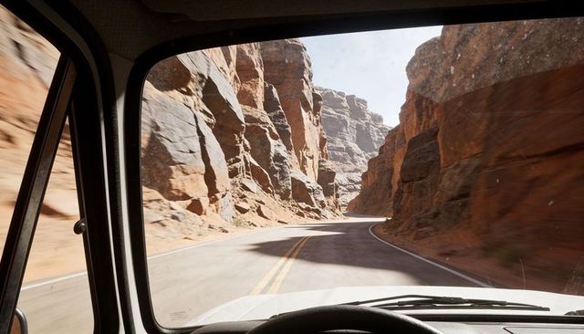 Driving winding red rock canyon road through windshield, steering wheel, sunlit cliffs