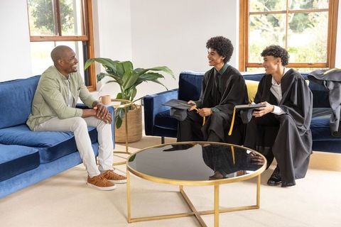 Diverse family celebrating home graduation with young male graduates in caps and gowns