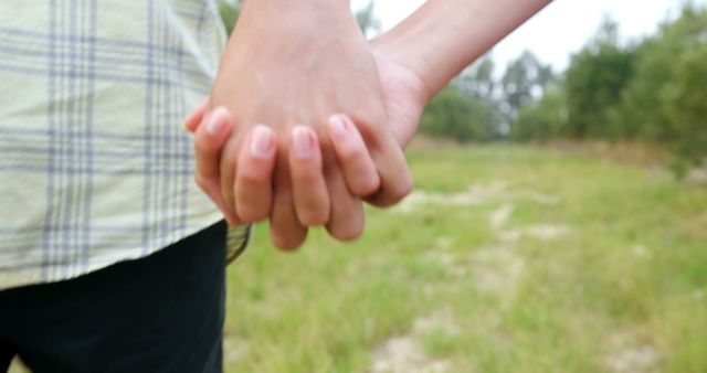 Two people are holding hands, symbolizing friendship or a romantic relationship, with copy space. Their gesture conveys a sense of closeness and companionship against a natural outdoor backdrop.