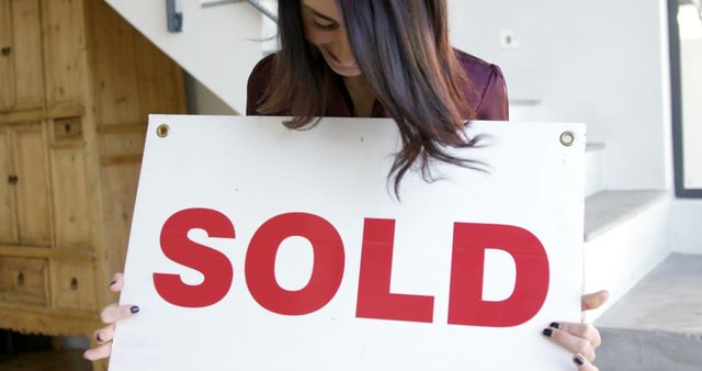 Joyful woman holding SOLD sign in new home - Download Free Stock Images Pikwizard.com