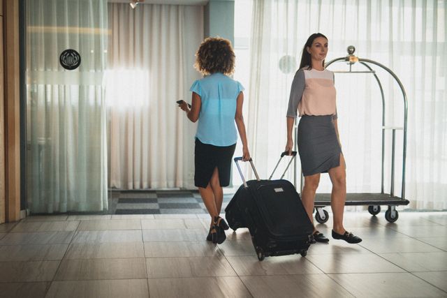 Two diverse female businesswomen walking through hotel lobby with suitcases. modern business travel hotel industry.