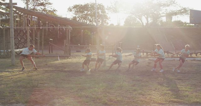 Children engaged in a tug of war competition, working together to pull a rope on a sunny day. This can be used to illustrate teamwork, fitness activities, team building exercises, or outdoor school activities.