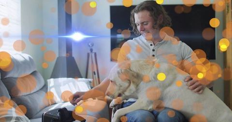 Young man holding labrador on couch cozy living room pet bonding with bokeh lights
