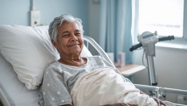 Reclining senior indian woman smiling in hospital bed with patient lift and soft daylight