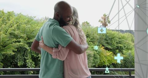 Mature interracial couple hugging on balcony with health overlays, tender senior embrace