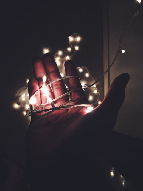 Hand holding glowing fairy lights in darkness creates a magical and serene atmosphere. Ideal for themes related to festivity, decoration, night, and creative lighting. Perfect for backgrounds, inspirational or festive projects, and adding an aesthetic touch to designs.