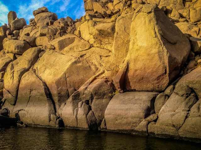 Golden rocks illuminated by the sunset by calm water, perfect for outdoor magazines, travel advertisements, or nature blogs. Adds a tranquil and serene element to designs, highlighting the beauty of natural landscapes.