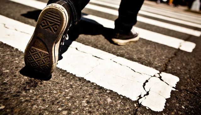 Walking across cracked zebra crosswalk closeup showing sneaker sole and urban asphalt