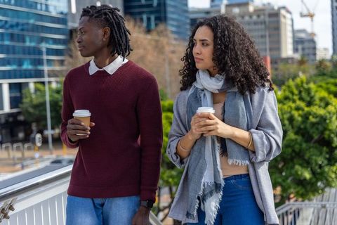 Young diverse friends holding takeaway coffee and chatting on modern urban overpass