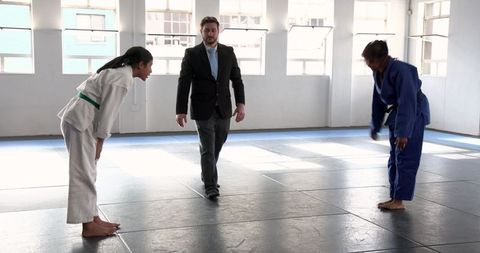 Martial arts competitors bowing on mats with referee overseeing