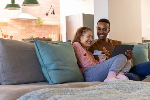 Diverse Couple Relaxing on Sofa with Tablet and Credit Card