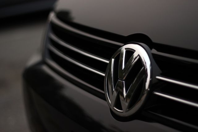 Close-up view of a Volkswagen car badge on a black grille. Ideal for use in automotive advertising, brand promotion, vehicle reviews, and related articles.