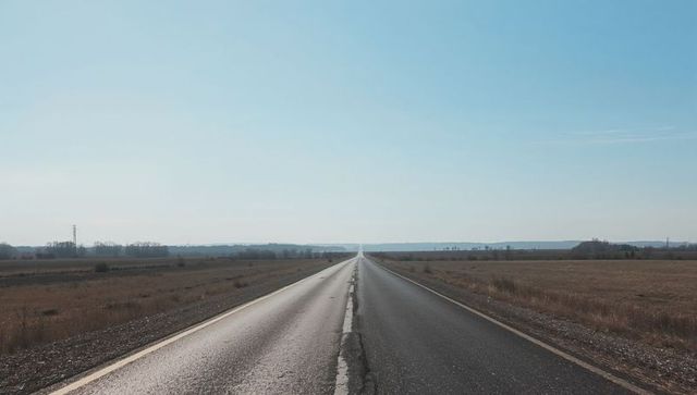 Endless straight country road leading toward horizon through wide open farmland
