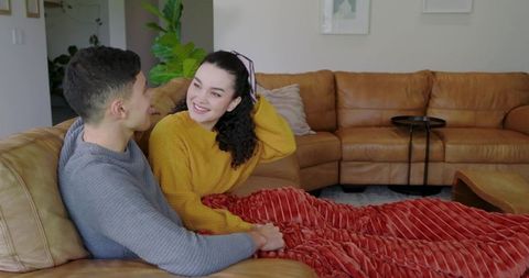 Diverse couple relaxing on cozy sofa with red blanket in modern living room
