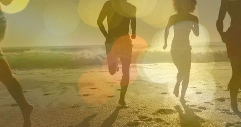 Friends running along sunlit shoreline at sunrise with lively lens flare and footprints