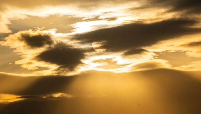 Golden sun disk peeking through layered clouds casting dramatic rays and amber glow
