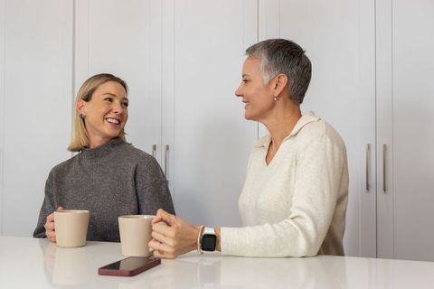 Mother and daughter sharing morning coffee, chatting and bonding in bright minimalist kitchen