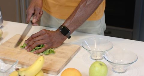 Mid-adult African American man chopping greens on wooden board with chef's knife