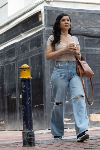 Adult woman walking sidewalk holding coffee cup wearing ripped jeans and leather satchel