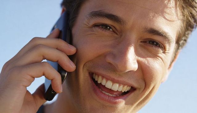 Sunlit young man smiling and talking on mobile phone closeup, candid outdoor portrait