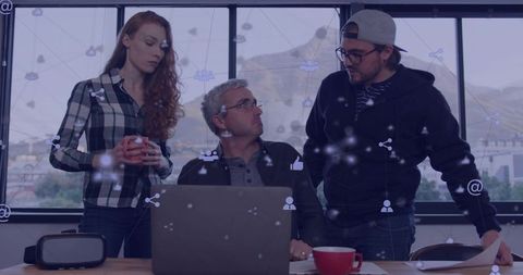 Three colleagues discussing project around laptop in modern office with mountain view