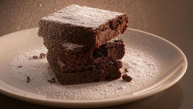 Fudgy chocolate brownies dusting powdered sugar in warm studio light