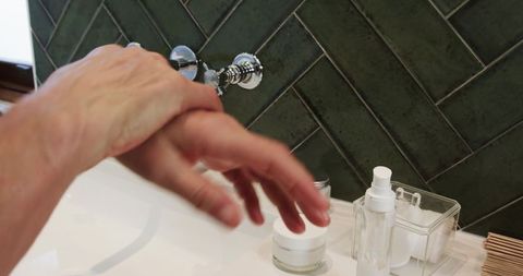 Rubbing lotion into skin by sink for skincare routine